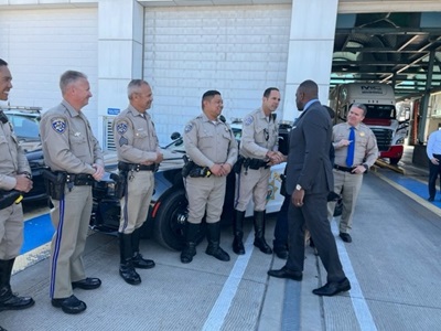 A group of CHP officers standing in front of a police vehicle waiting to shake hands with Secretary Omishakin