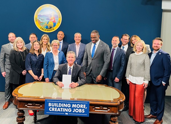 Group of people standing around Governor Newsom, sitting at a desk, holding up a signed document